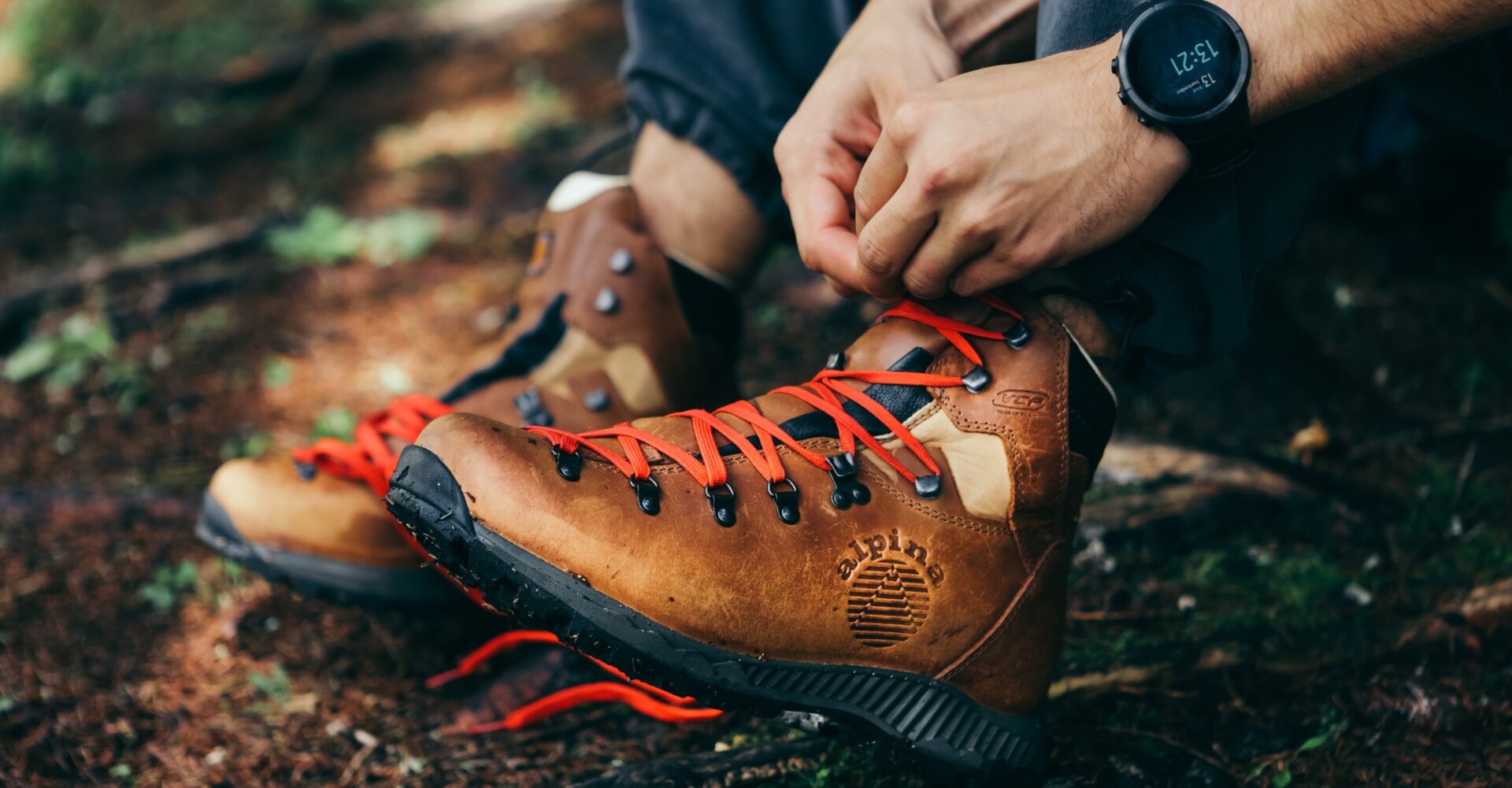 Hiker tying red laces on leather Alpina hiking boots